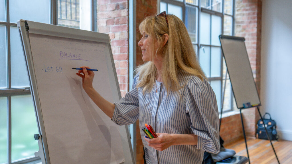Emma writing let go on a whiteboard and balance at a reconnect coaching workshop